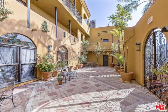 Outdoor lobby area with seating and potted plants, surrounded by a multi-story building.