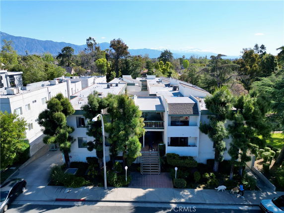 Front view of a multi-story residential building with trees and a staircase entrance.