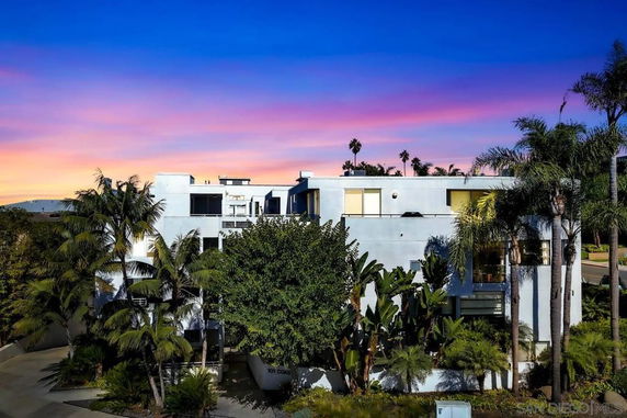 Front view of a multi-story modern building with palm trees in front.