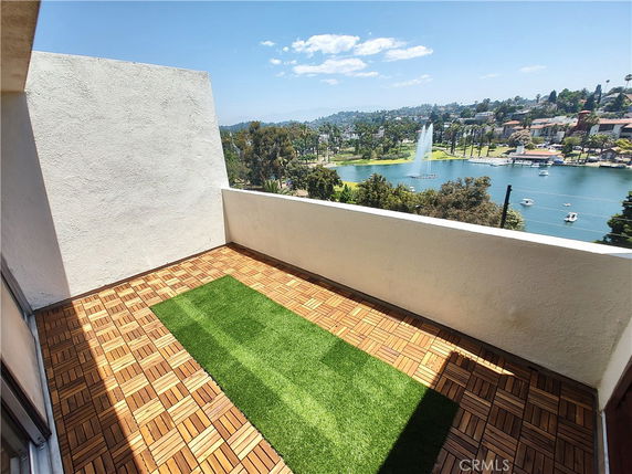 View from a patio with wooden flooring and artificial grass overlooking a lake with a fountain.