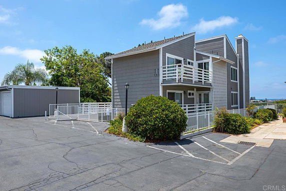 Front view of a multi-story building with balconies and an adjacent parking area.