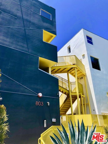 Front view of a modern multi-story building with geometric design and vibrant yellow accents.