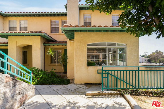 Front view of a two-story house with beige walls and green accents, featuring a large window and a small porch.