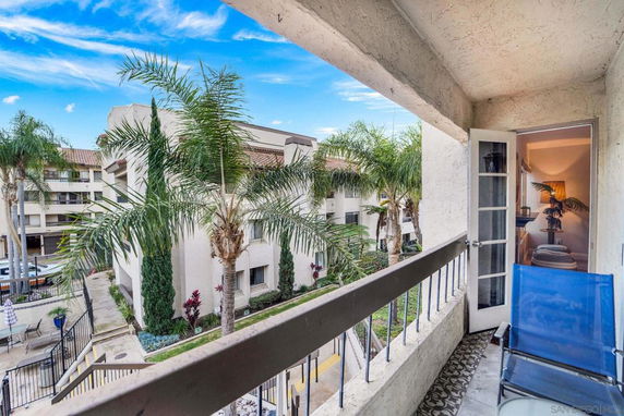 View from a balcony of a residential building showing adjacent apartment buildings and palm trees.