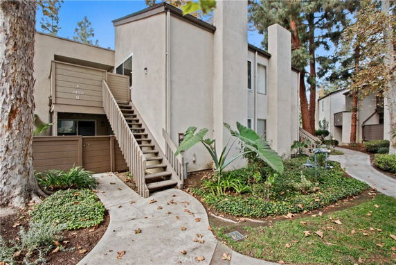 Front view of a two-story residential building with external staircase and surrounding trees.