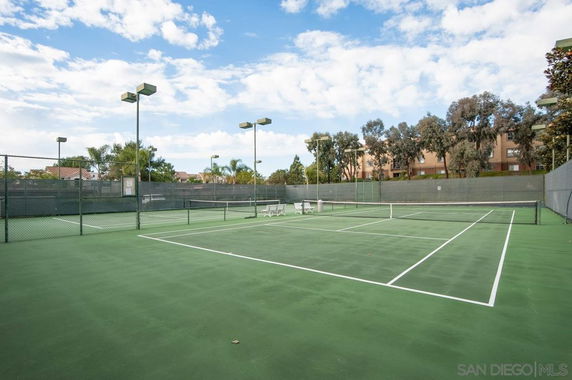 Outdoor tennis court with green flooring and surrounding fence.