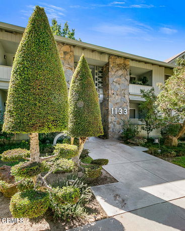 Front view of a house with stone facade and unique topiary bushes in the foreground.