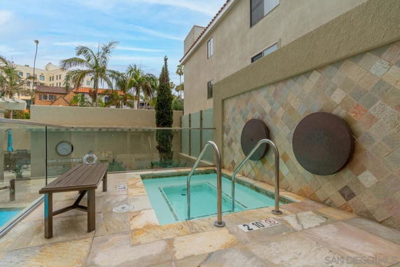 Outdoor area with a small jacuzzi surrounded by a glass barrier and tiled walls.