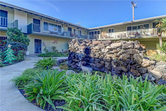 Outdoor view of a two-story apartment complex with a central courtyard featuring a rock waterfall and greenery.