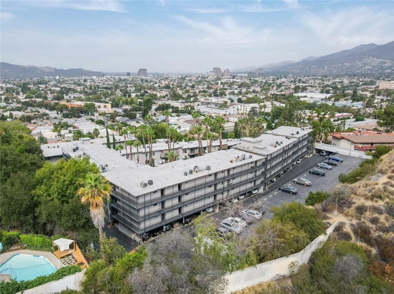 Aerial view of a large multi-story building surrounded by a cityscape, with parking and greenery visible.