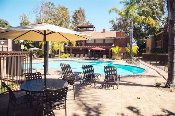Outdoor swimming pool area with lounge chairs and a table with an umbrella.