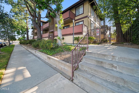 Front view of a multi-story apartment building with trees and a sidewalk.