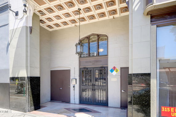 Front elevation of a building entrance with decorative ceiling and metal gate.