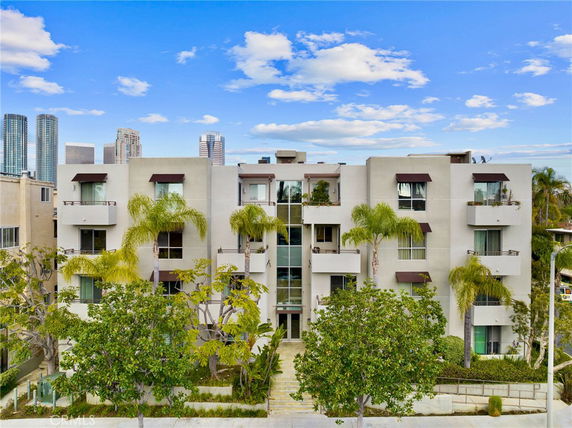 Front view of a modern multi-story apartment building with balconies and surrounding trees.