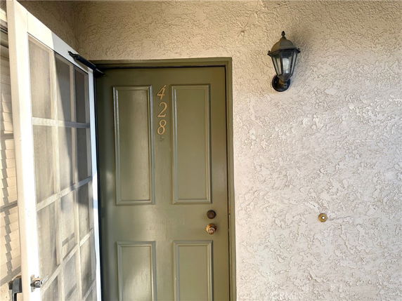 Front view of a building entrance with a green door and a wall-mounted light fixture.