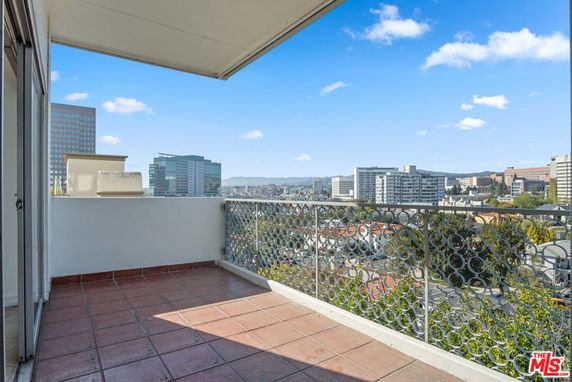 Balcony view overlooking a cityscape with multiple buildings and a clear blue sky.