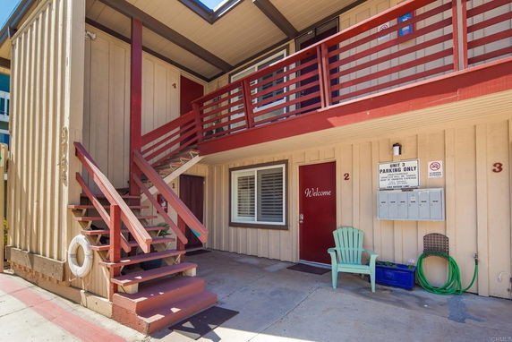 Exterior view of a multi-unit residential building with red wooden railings and beige siding.