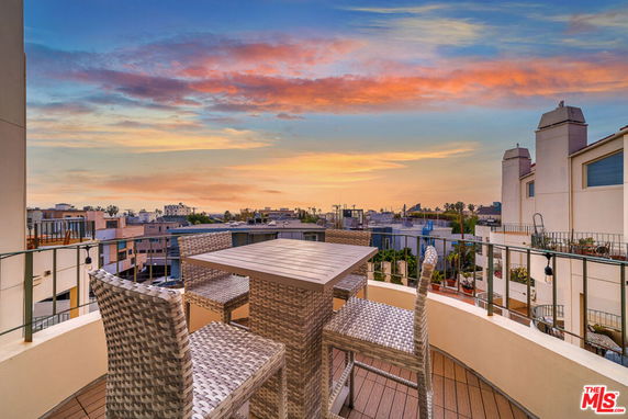 Rooftop seating area with wicker chairs and a view of surrounding buildings at sunset.