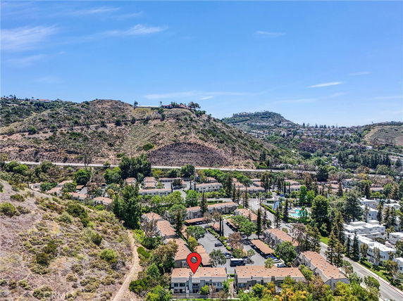 Aerial view of residential buildings surrounded by hills and trees.