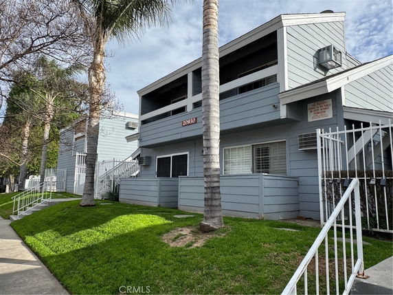 Front view of a two-story residential building with balconies and fenced entrance.