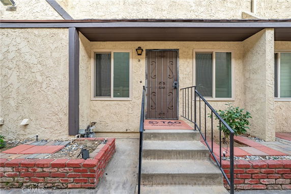Front view of a house entrance with a metal door, concrete steps, and brick planters.