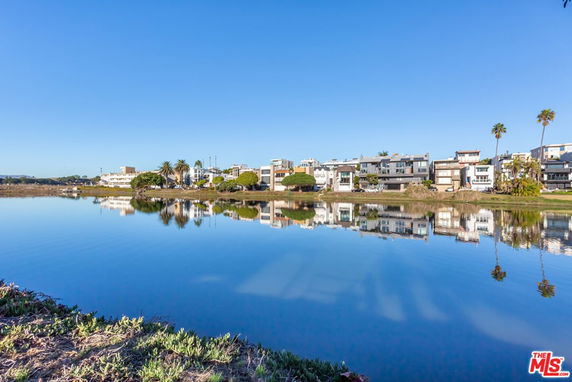 Panoramic view of a waterfront with modern buildings and palm trees reflecting in the water.
