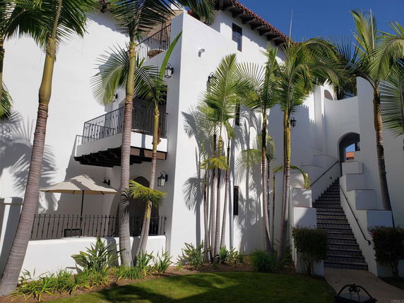 Front view of a white multi-story house with balconies and outdoor stairs.