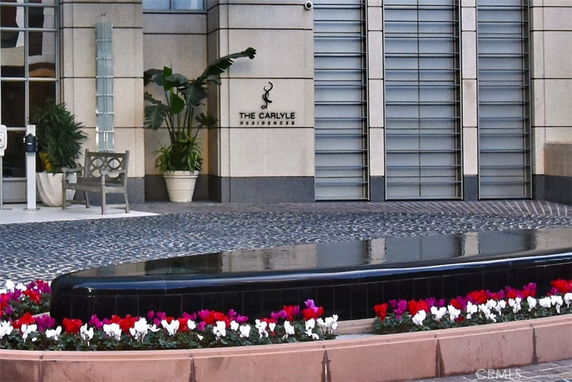 Front view of a building entrance with a sign reading 'The Carlyle Residence' and a decorative fountain with flowers.