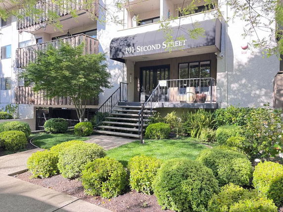 Front view of a multi-story building entrance with stairs and landscaping.