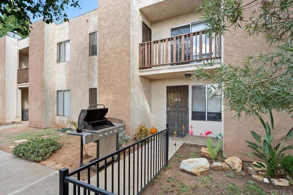 Front view of a two-story apartment building with balconies and a small fenced yard.