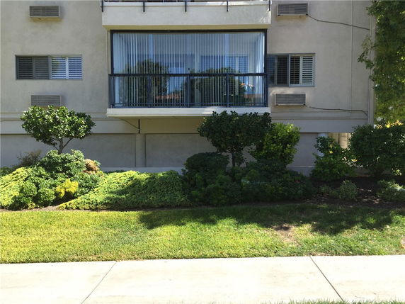 Front view of a building with a balcony and plants in the foreground.