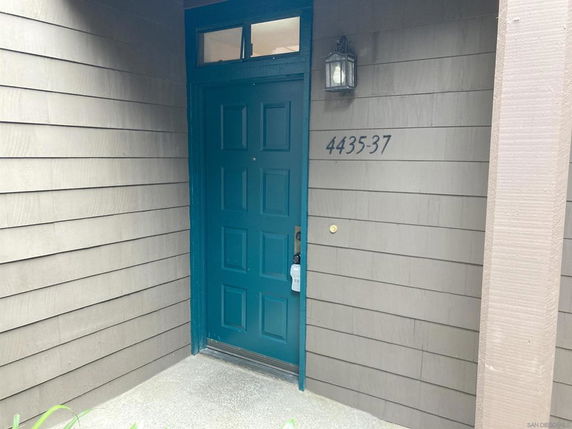 Entrance view of a building with a teal door and wall lamp.