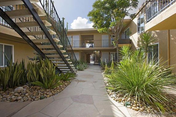 Front view of a two-story apartment building with an outdoor staircase and landscaped pathway.