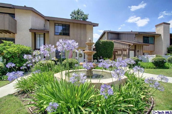 Front view of a multi-story residential building with a fountain and landscaped garden.