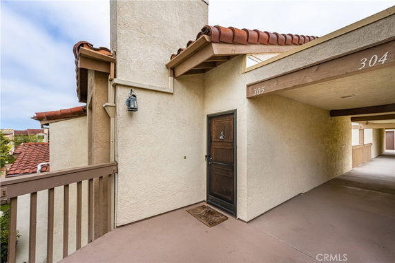 Exterior view of an apartment entrance with a wooden door and overhanging roof.