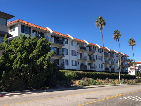 Front view of a multi-story apartment building with balconies and a tiled roof.