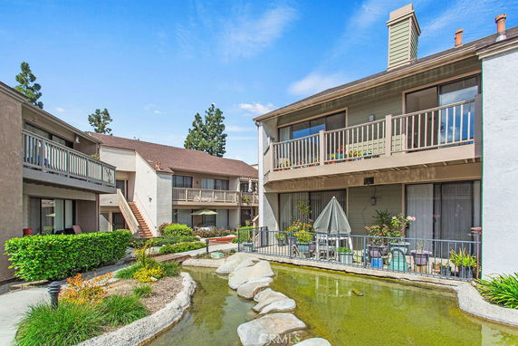 Front view of a residential building with balconies and a small pond in the foreground.