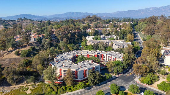 Aerial view of a multi-story residential complex surrounded by trees and roads, with mountains in the background.