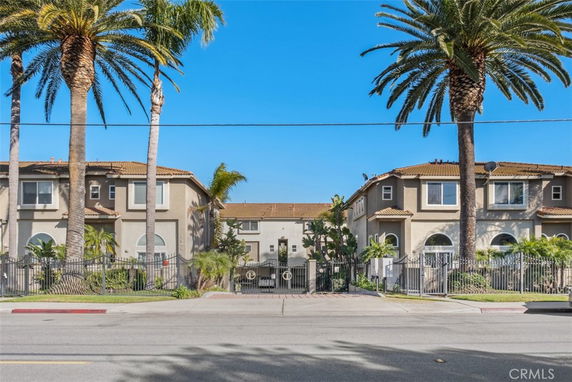 Front view of a multi-story residential building with palm trees and gated entrance.