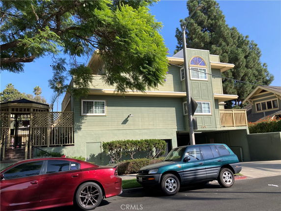 Front view of a multi-story building with a small balcony and surrounding trees.