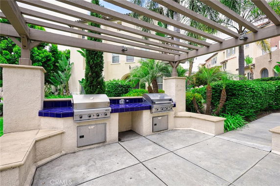 Outdoor grilling area with built-in barbecue grills and pergola overhead.