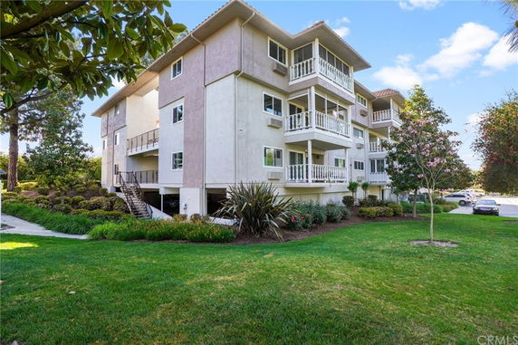 Front view of a multi-story residential building with balconies and surrounding greenery.