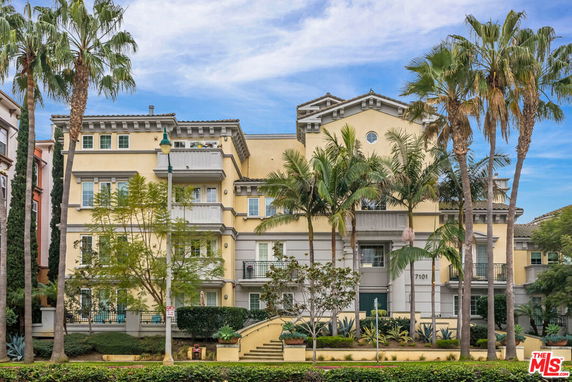 Front view of a multi-story residential building with balconies and palm trees in front.