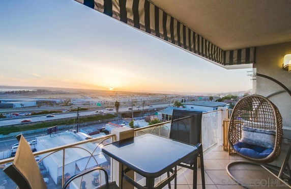 Balcony view overlooking a cityscape with a highway, buildings, and sunset in the distance.