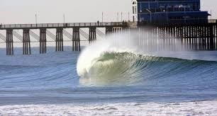 Ocean wave with a pier in the background.