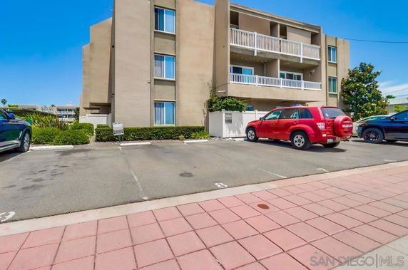 Parking area in front of a multi-story building with balconies.