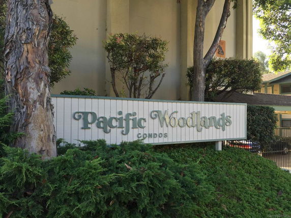 Front view of a building with a sign reading 'Pacific Woodlands Condos'.