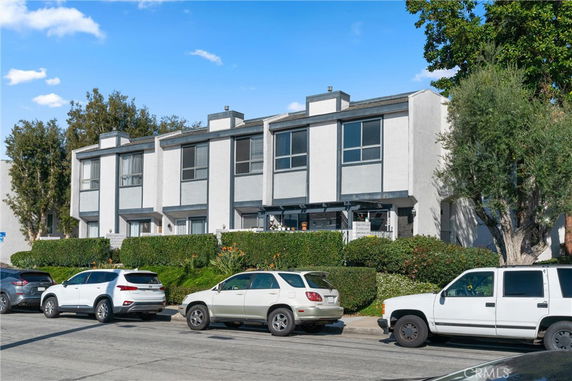 Front view of a multi-story residential building with large windows and a hedge in front.