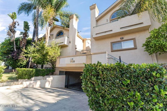 Front view of a multi-story residential building with palm trees and a gated driveway.