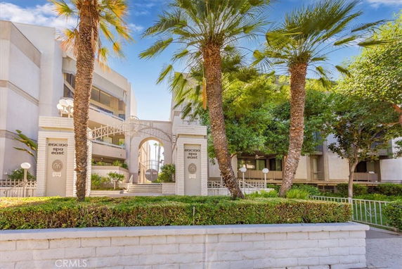 Front view of a multi-story residential building with arches and palm trees.